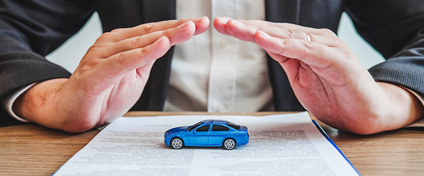 Two hands cupped over a small blue toy car sitting on a printed insurance policy.