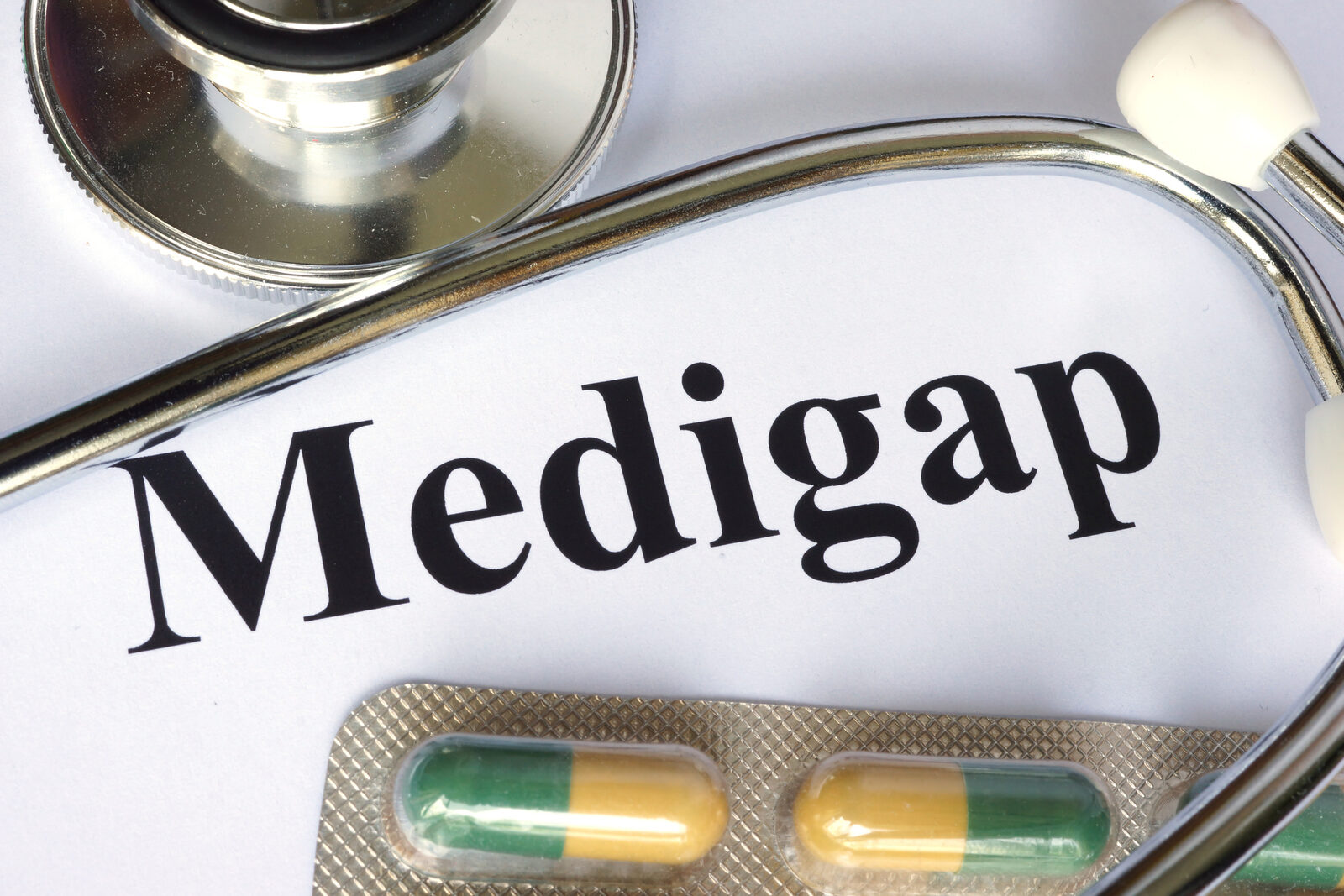 The word Medigap printed on white paper beneath a stethoscope, with a blister pack of capsules below.
