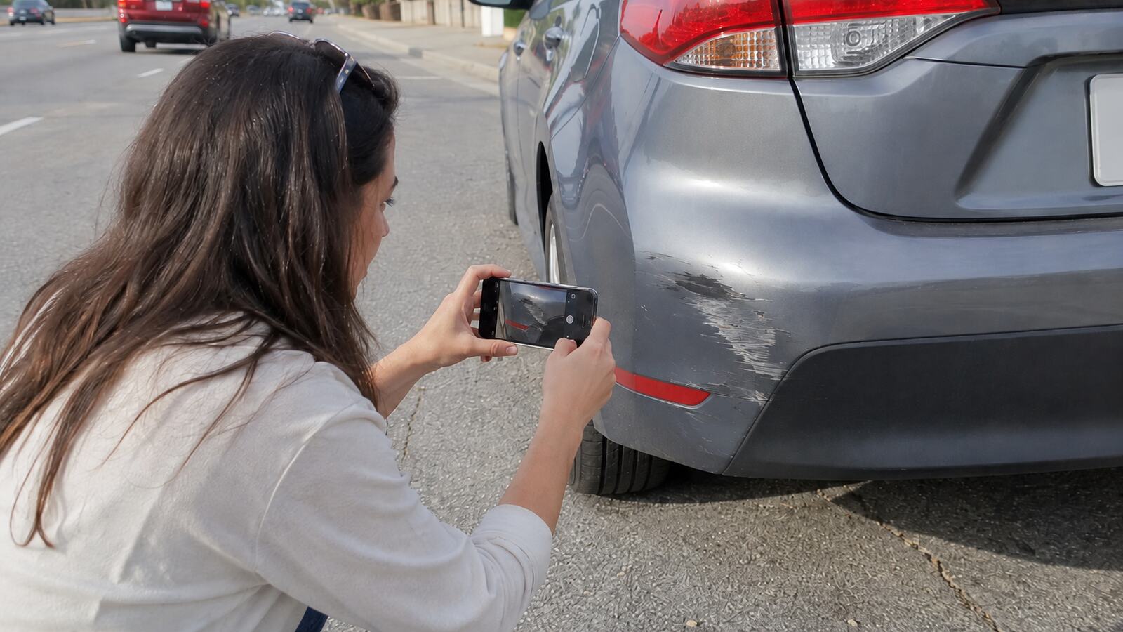 A person photographing damage to a car bumper with a phone after a collision.