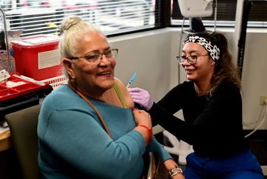 An older woman receiving a vaccination from a nurse at a clinic.