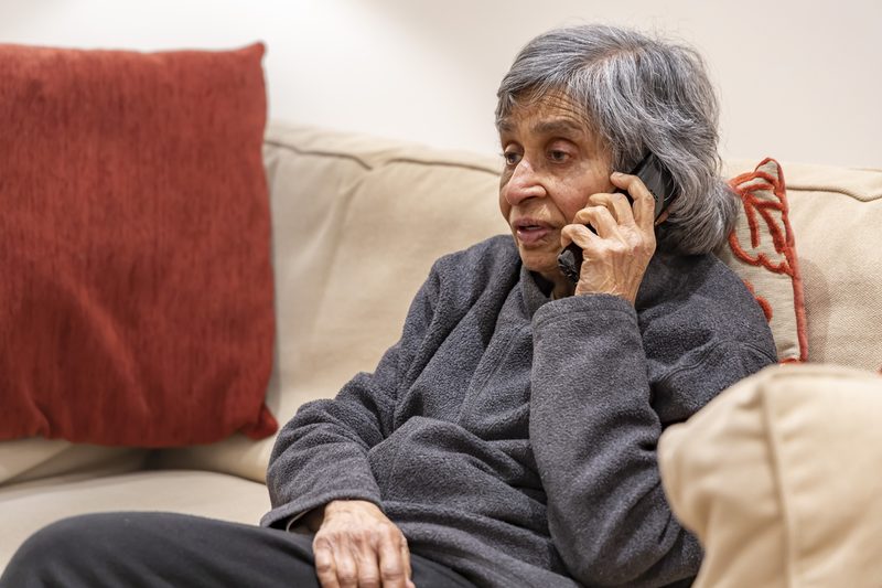 An older woman sitting on her sofa talking on the phone.