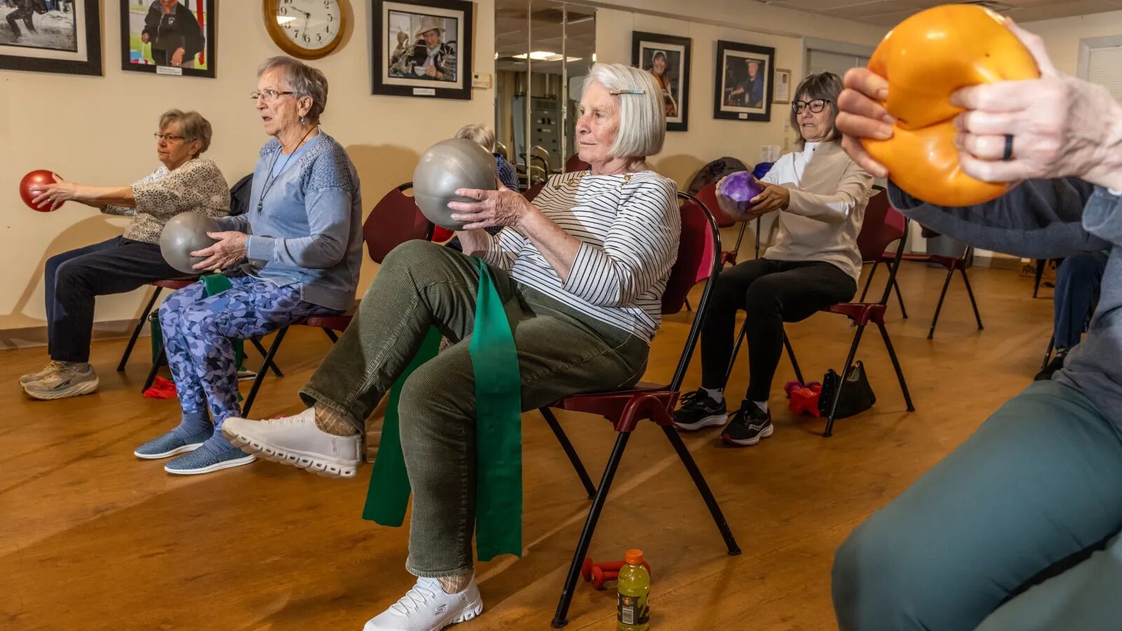 A group of seniors in a seated exercise class lift rubber balls and stretch resistance bands.
