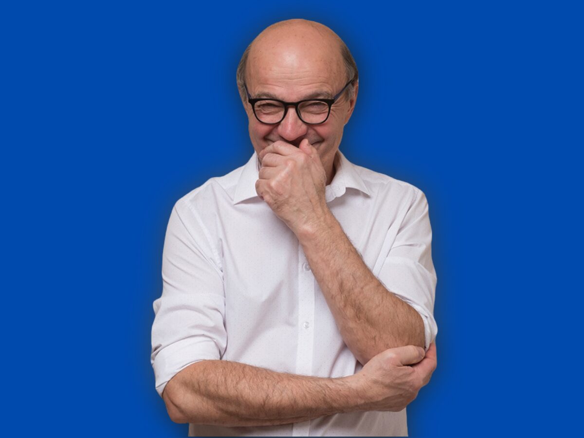 A smiling man with glasses in a white shirt, arms folded, against a bright blue background.