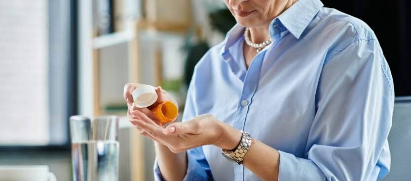 A woman in a light blue shirt pours pills from an orange bottle into her palm.